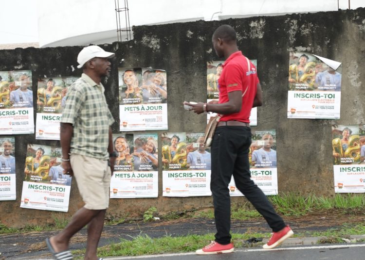 Deux passants dans une rue abidjanaise, à côté d'un mur d'affiches de campagne de sensibilisation de la CE