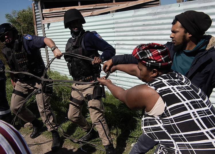 Des membres de la police métropolitaine du Cap tentent d'arracher un morceau de fil électrique branché illégalement à des habitants d'un quartier informel appelé Oasis Farm, près du Cap, le 13 septembre 2023.
(Photo de RODGER BOSCH / AFP)