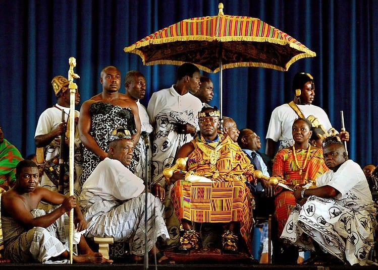 Ashanti King Asantehene Otumfuo Tutu II (C) sits on his throne, surrounded by his entourage during the traditional Ghanaian Durbar celebration in Amsterdam, 22 June 2002. The king, who is on week-long visit to the Netherlands, was received by the Ghanaian community in the Dutch capital. (Photo by ROBIN UTRECHT / ANP / AFP)