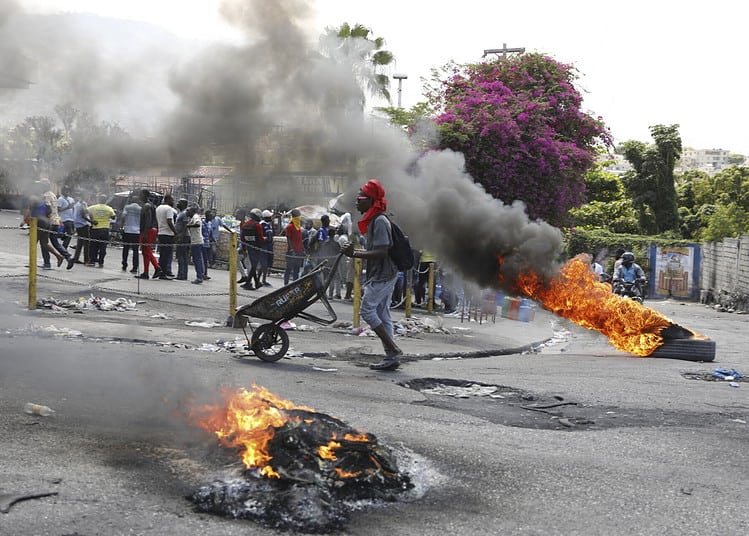A man pushes a wheelbarrow past burning tires during a protest demanding the resignation of Prime Minister Ariel Henry, in Port-au-Prince, Haiti, Thursday, March 7, 2024. (AP Photo/Odelyn Joseph)