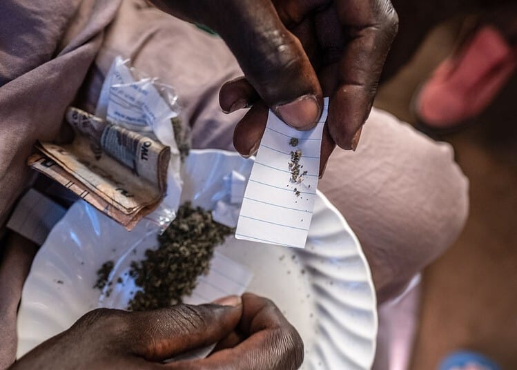 A kush dealer measures out a portion of kush, which will be wrapped in a paper packet and sold for as little as 5,000 Leones (roughly $0.25), in a slum neighbourhood in Freetown, Sierra Leone, on the 24th of September 2023.