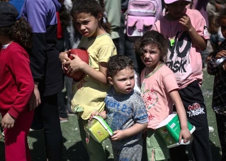 Palestinians wait in front of a free food distribution point to receive their portion of a hot meal, at the Nuseirat refugee camp in the central Gaza Strip on April 19, 2025. (Photo by Eyad BABA / AFP)