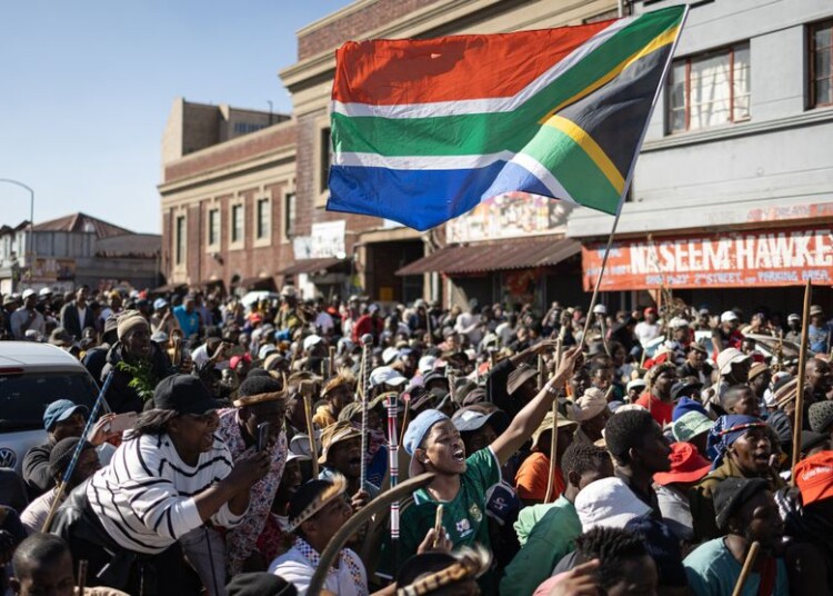 Protesters gather as one of them waves a South African flag during a protest march against undocumented migrants in Springs, Ekurhuleni, on June 8, 2026. Hundreds of anti-migrant protesters marched through a township outside Johannesburg on June 8, 2026, a day after South African President Cyril Ramaphosa pledged action against groups accused of fuelling xenophobic violence.
South Africa has seen recurring bouts of anti-migrant violence, with protests intensifying this year after vigilante groups ordered undocumented foreigners to leave by June 30. (Photo by EMMANUEL CROSET / AFP)